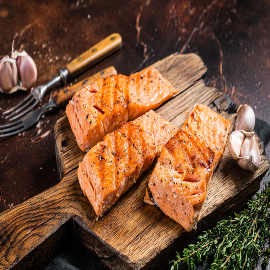 Griiled salmon fillets, fish steaks on wooden board with thyme. Dark background. Top view.